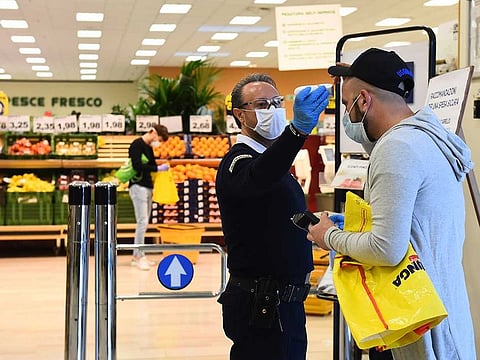 A worker checks the temperature of a customer at the entrance of a supermarket, as the spread of the coronavirus disease (COVID-19) continues, in Turin, Italy, April 14, 2020.