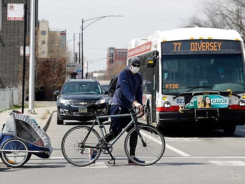 A man wears a mask as he crosses the street with his bicycle in Chicago, Saturday, April 11, 2020. There is no end in sight for the stay-at-home order during the COVID-19 pandemic as Chicagoans fight summer weather temptations. 