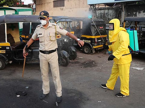 A civic worker sprays disinfectant on a policeman standing guard after a protest by migrant workers against the extension of the lockdown, in a slum in Mumbai, India, Tuesday, April 14, 2020.