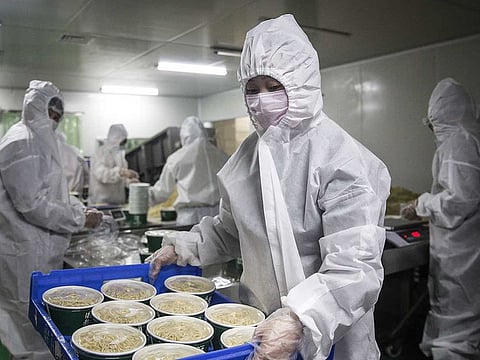 A worker wearing a protective suit, masks and gloves prepares to carry a tray of hot dry noodles packed into containers at a noodle factory in Wuhan, Hubei Province, China, on Tuesday, April 7, 2020. 