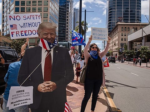 A Trump cutout with a US flag around its neck is seen next to protesters rallying in downtown San Diego against California's stay at home order to prevent the spread of the novel coronavirus, on April 18, 2020. Hundreds protested Saturday in cities across America against coronavirus-related lockdowns - with encouragement from President Donald Trump - as resentment grows against the crippling economic cost of confinement.  