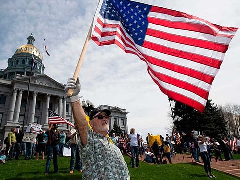 A man waves a US flag in front of the Colorado State Capitol building 