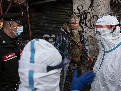 Medical workers wearing full body protective clothes speak with a rough sleeper while on patrol with the Carabinieri in Milan, Italy. 
