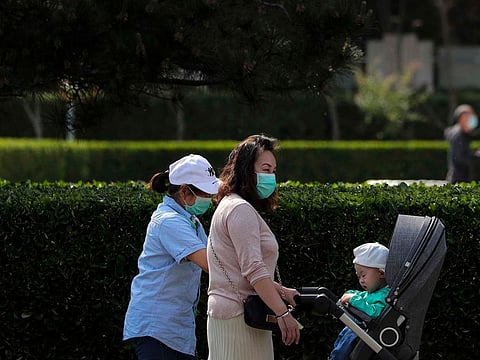 Women wearing protective face masks to help stop the spread of the new coronavirus push a child on a stroller along a street in Beijing, Sunday, April 26, 2020.
