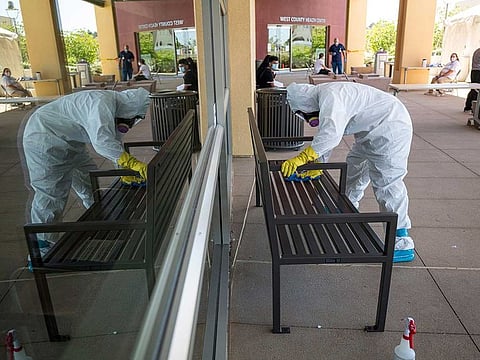 A worker wearing a hazmat suit disinfects a bench at a COVID-19 walk-in testing site in San Pablo, California, US, on Tuesday, April 28, 2020. California, which has closed schools for the academic year, is considering bumping up the start of the new school year to late July or early August, Governor Gavin Newsom said.