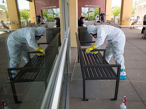 A worker wearing a hazmat suit disinfects a bench at a COVID-19 walk-in testing site in San Pablo, California, US, on Tuesday, April 28, 2020. California, which has closed schools for the academic year, is considering bumping up the start of the new school year to late July or early August, Governor Gavin Newsom said.