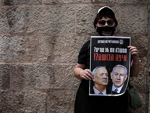 A woman wears a mask for protection against the spread of the coronavirus holds a sign that reads: 'a government with 36 ministers? Where is the shame?'" in Jerusalem, Sunday, May 3, 2020.