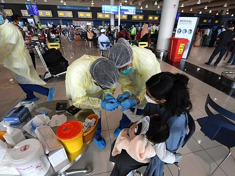 Health workers test an Indian child held by a woman at the Dubai International Airport 