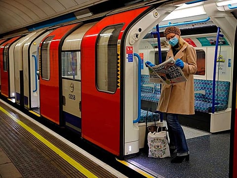 A woman wearing PPE (personal protective equipment), including a face mask as a precautionary measure against COVID-19, reads a newspaper as she stands aboard a London Underground Tube train, in the morning rush hour on May 11, 2020, as life in Britain continues during the nationwide lockdown due to the novel coronavirus pandemic. 