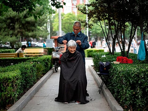 A barber cuts the hair of an elderly woman at a public park in Beijing on May 13, 2020. 