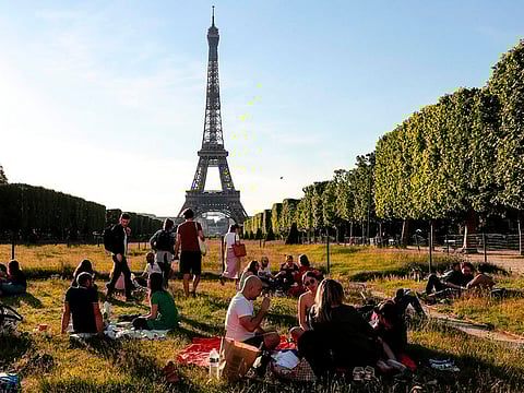 People sit on the Champs de Mars at sunset in front of the Eiffel Tower, on May 17, 2020, in Paris. The sonic boom of a fighter jet breaking the sound barrier reverberated across the city on Wednesday.
