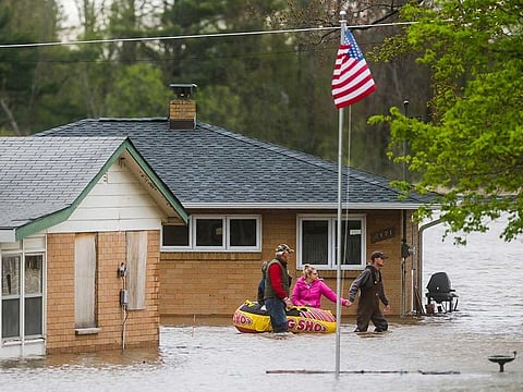People help each other travel from one home to another using an inflatable raft on Oakridge Road on Wixom Lake, Tuesday, May 19, 2020 in Beaverton, Michigan. People living along two mid-Michigan lakes and parts of a river have been evacuated following several days of heavy rain that produced flooding and put pressure on dams in the area. 