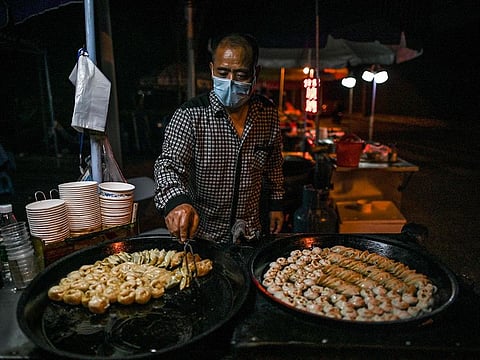 A man wearing a facemask sells food at his stall on a street in Wuhan, China’s central Hubei province on May 20, 2020.