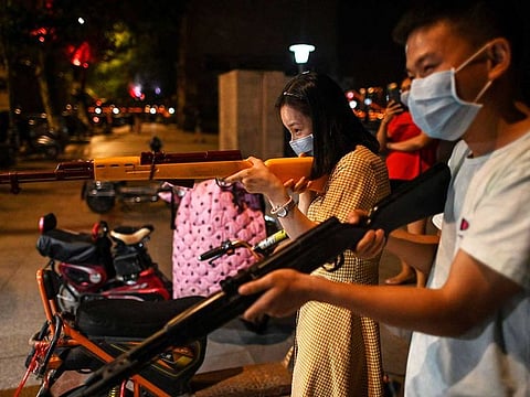 A couple tries to burst balloons with toy guns at a night stall along the Yangtze River in Wuhan in China’s central Hubei province on May 19, 2020. 