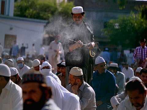 A man sprays disinfectant among worshippers attending an Eid Al Fitr prayer at a ground in Rawalpindi, Pakistan, Sunday, May 24, 2020.