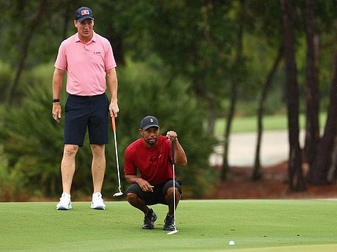 Tiger Woods lines up a putt as Peyton Manning looks on