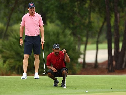 Tiger Woods lines up a putt as Peyton Manning looks on
