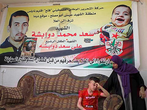 Ahmed Dawabsheh, the survivor of the arson attack that killed his parents and 18-month-old brother, sits under a poster portraying his family members at his grandparents home in the Israeli occupied West Bank village of Duma on May 18, 2020. An Israeli court convicted Jewish colonist Ben Uliel on three counts of murder over the attack in 2015. 