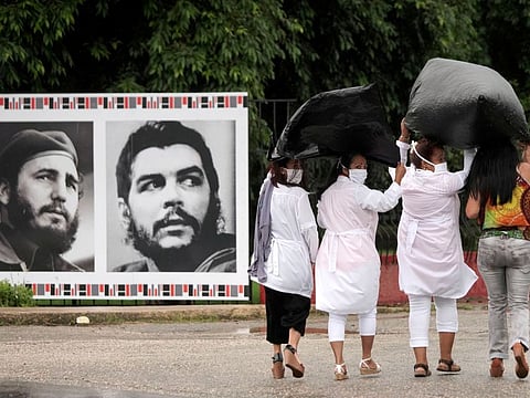 Cuban doctors, protecting themselves from the rain with plastic bags, pass by images of Cuban late President Fidel Castro and late revolutionary hero Ernesto "Che" Guevara after a farewell ceremony before departing to Kuwait to assist, amid the coronavirus disease (COVID-19) outbreak, in Havana, Cuba June 4, 2020.  