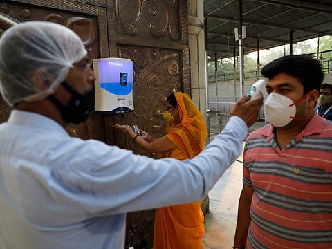 A woman sanitizes her hands as a man gets his temperature checked inside a temple after the opening of most religious places after India eased lockdown restrictions that were imposed to slow the spread of the coronavirus disease (COVID-19), in New Delhi, India, June 8, 2020. 