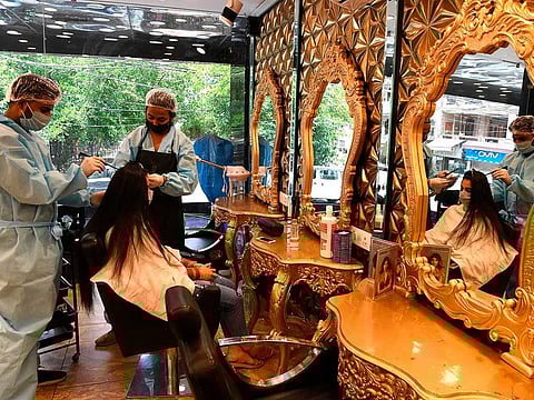 Hairdressers wearing personal protective equipment (PPE) attend to a customer (C) at a hair salon, after the government eased a  nationwide lockdown as a preventive measure against the COVID-19 coronavirus, in New Delhi on June 9, 2020. 