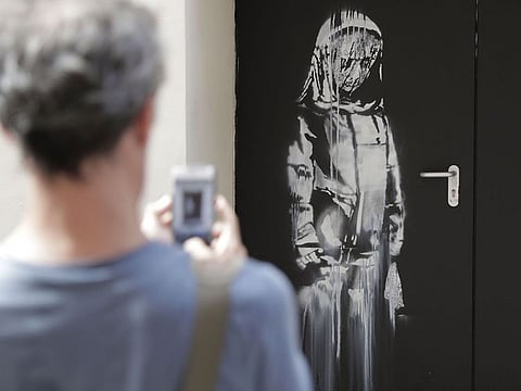 A man takes a photograph of an artwork by street artist Banksy in Paris on a side street to the Bataclan concert hall where a terrorist attack killed 90 people on Novembre 13, 2015. The stolen Banksy work has been found in Italy,