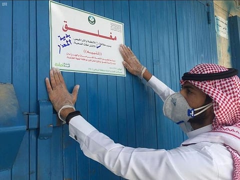 A Saudi municipal official pastes a temporary closure notice on the door of a store in Riyadh for violating precautions against coronavirus. 