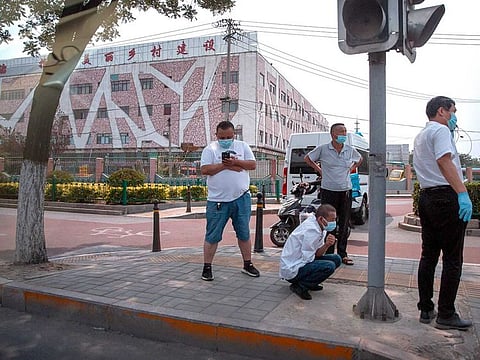 People wearing face masks to protect against the new coronavirus stand along a street outside the Xinfadi wholesale food market district in Beijing, Saturday, June 13, 2020. Beijing closed the city's largest wholesale food market Saturday after the discovery of seven cases of the new coronavirus in the previous two days. 