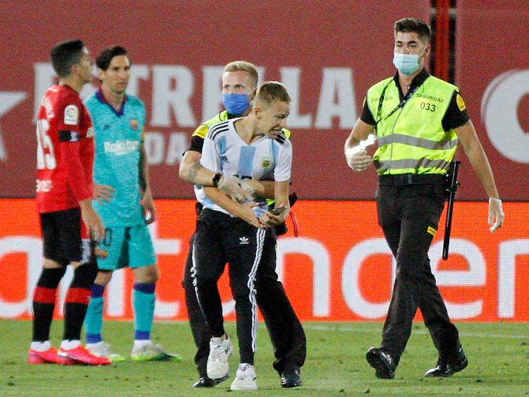 The supporter invades the pitch with Barcelona's Lionel Messi behind him.