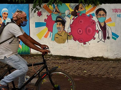 A man wearing a mask pedals his bicycle past a graffiti on a wall (File) 
