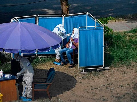 A health official (top L) wearing personal protective equipment (PPE) takes a sample from a man sitting in a temporary cabin at a drive-through screening and testing facility for the COVID-19 coronavirus, alongside a street in Islamabad on June 7, 2020. 