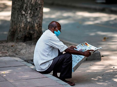 A man reads a newspaper sitting in front of closed shop at a market area in New Delhi.