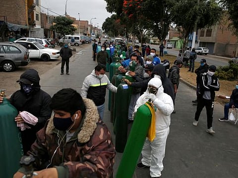 People wearing face masks wait with oxygen tanks at a private distributor that recharges tanks, amid the spread of the coronavirus disease (COVID-19), in Lima, Peru June 25, 2020.