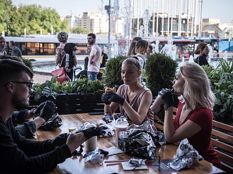 Customers wearing gloves eat burgers on the terrace of Black Star Burger in Moscow on June 16, 2020.  Status-conscious fast-food joints across Eastern Europe have offered their diners disposable gloves for years and the idea may find a wider audience in the pandemic era. (Sergey Ponomarev/The New York Times)
