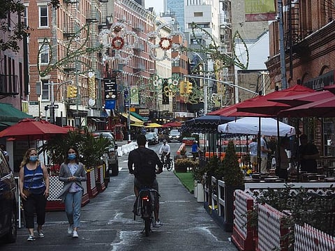 People wearing protective masks walk down a street lined with outdoor seating for restaurants in the Little Italy neighborhood of New York, US, on Monday, July 6, 2020. New York City delayed the return of indoor dining, which had been planned for July 6, as other states experience a spike in COVID-19 cases after reopening their restaurants and bars.