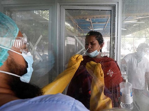 A paramedic wearing protective gear takes a nasal swab of a woman at a glass booth, to be tested for the coronavirus disease (COVID-19), in Karachi, Pakistan.