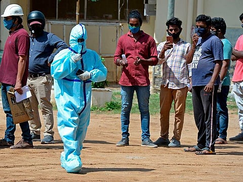 A health worker wearing Personal Protective Equipment (PPE) gear walks past residents standing in queue to register their names at a free testing centre for the COVID-19 coronavirus, at Medchal–Malkajgiri district on the outskirts of Hyderabad July 21, 2020. A man in Andhra Pradesh threw the body of his stillborn child in a canal after village elders did not allow him to perform the last rites in the village fearing the baby had coronavirus.