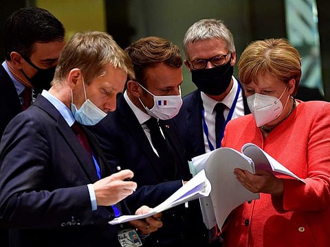 Spain's Prime Minister Pedro Sanchez (L), French President Emmanuel Macron (C) and German Chancellor Angela Merkel (R) look into documents during an EU summit in Brussels on July 20, 2020, as the leaders of the European Union hold their first face-to-face summit over a post-virus economic rescue plan. 