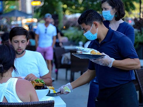 A waiter wearing a protective mask serves food to patrons at the outdoor seating area of a restaurant in Chicago, Illinois, US, on July 24, 2020. 