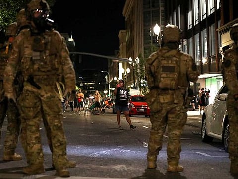 A woman standing in front of federal law enforcement officers holds a camera during a protest against racial inequality and police violence in Portland, Oregon, U.S., July 29, 2020.