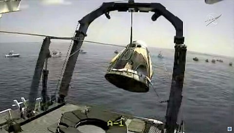 SpaceX’s Crew Dragon capsule is hoisted onto its recovery ship with the astronauts inside, while a gaggle of private vessels gawk around the perimeter of the landing zone in the Gulf of Mexico. 