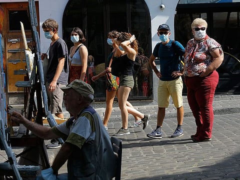 A painter works while tourists stroll in the Montmartre district Monday, Aug. 10, 2020 in Paris. 