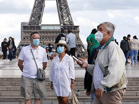 People wearing protective masks stand at the Trocadero square near the Eiffel Tower, in Paris.