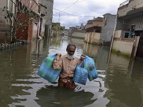File photo: A man carries goods as he wades through flooded street after heavy monsoon rains, in Karachi. 