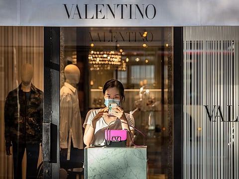 An employee wearing a protective face mask uses her mobile phone next to a handbag in a Valentino SpA clothing store on Paseo de Gracia in Barcelona, Spain, on Wednesday, Aug. 26, 2020. 