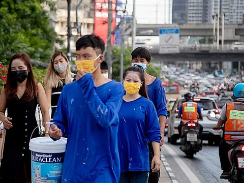 Office workers and construction workers with face masks walk in a side walk in Bangkok, Thailand.