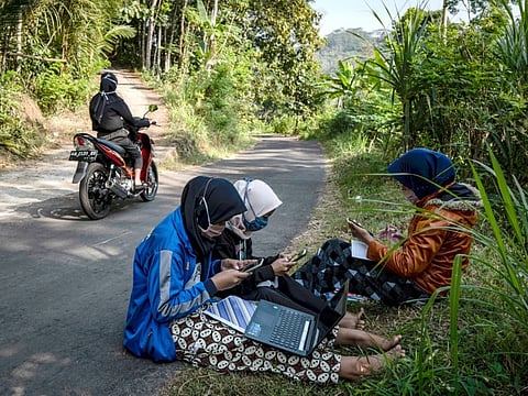 Teara Noviyani, 19; Siti Salma, 13; and Fitri Zahrotul, 15, studying on the side of a road in Kenalan, Indonesia. The cell reception is strong enough there to download their school assignments.