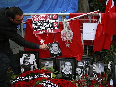 In this January 4, 2017 file photo, a man adjusts a victim's photograph displayed with floral tributes and Turkish flags, outside the Reina night club following the New Year's day attack, in Istanbul.  