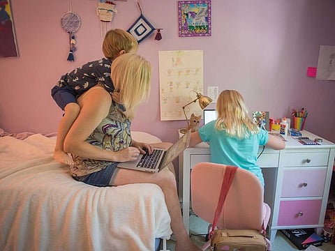 A mother works from home while her toddler son plays and her daughter works on a laptop computer during the first day of elementary school remote learning classes in New York