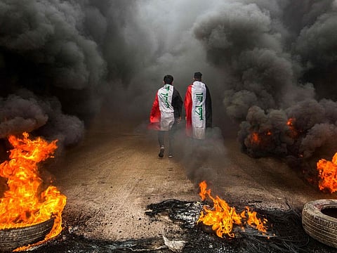 In this file photo taken on November 17, 2019, anti-government protesters draped in Iraqi national flags walk into clouds of smoke from burning tyres during a demonstration in the southern city of Basra.